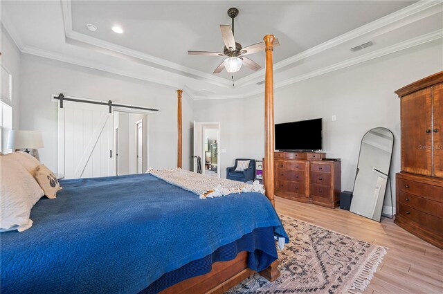 bedroom featuring light hardwood / wood-style floors, a barn door, a raised ceiling, ceiling fan, and ornamental molding