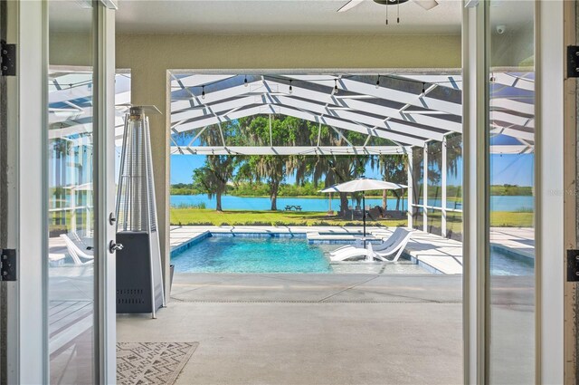 view of swimming pool featuring a patio, a water view, ceiling fan, and glass enclosure