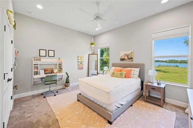 bedroom with a water view, ceiling fan, and light colored carpet