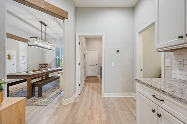 kitchen featuring light stone counters, light hardwood / wood-style flooring, decorative light fixtures, backsplash, and white cabinetry