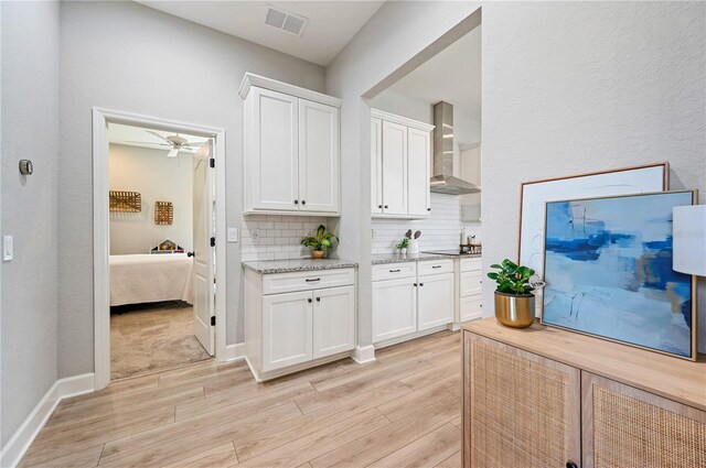 kitchen featuring white cabinets, wall chimney exhaust hood, light hardwood / wood-style flooring, decorative backsplash, and ceiling fan