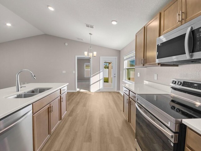 kitchen featuring pendant lighting, sink, vaulted ceiling, appliances with stainless steel finishes, and light hardwood / wood-style floors