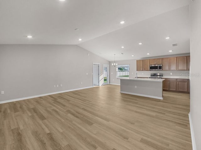 kitchen with light wood-type flooring, decorative light fixtures, vaulted ceiling, a center island with sink, and appliances with stainless steel finishes