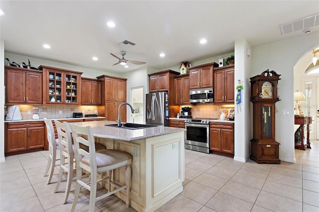 kitchen featuring tasteful backsplash, ceiling fan, a kitchen island with sink, appliances with stainless steel finishes, and sink