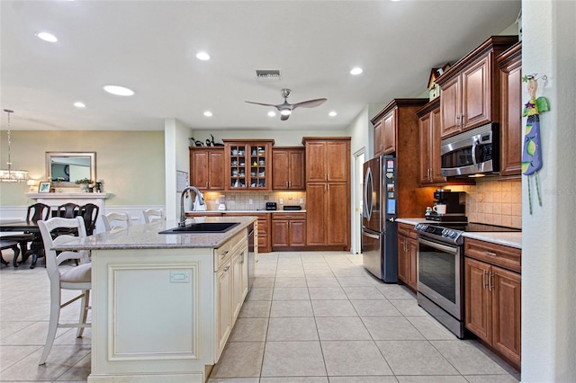 kitchen featuring ceiling fan with notable chandelier, stainless steel appliances, backsplash, a center island with sink, and sink