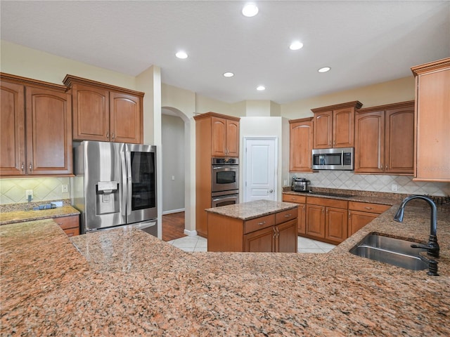 kitchen featuring stainless steel appliances, a center island, sink, backsplash, and light stone counters