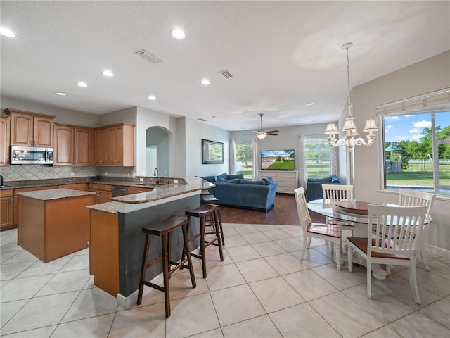 kitchen featuring light tile floors, appliances with stainless steel finishes, tasteful backsplash, and ceiling fan with notable chandelier