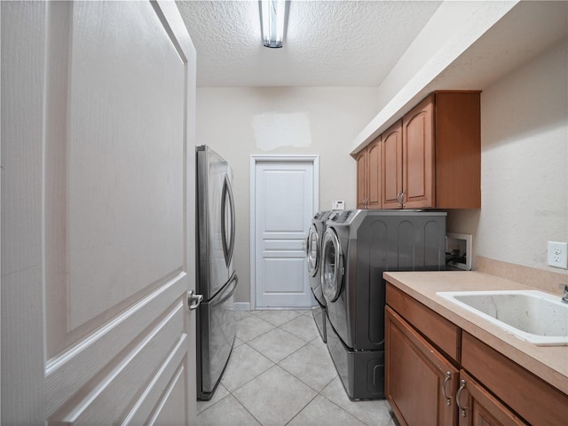 laundry area with cabinets, independent washer and dryer, sink, light tile flooring, and a textured ceiling