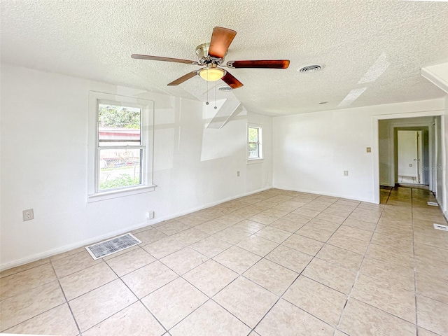 spare room with a textured ceiling, light tile patterned floors, and ceiling fan