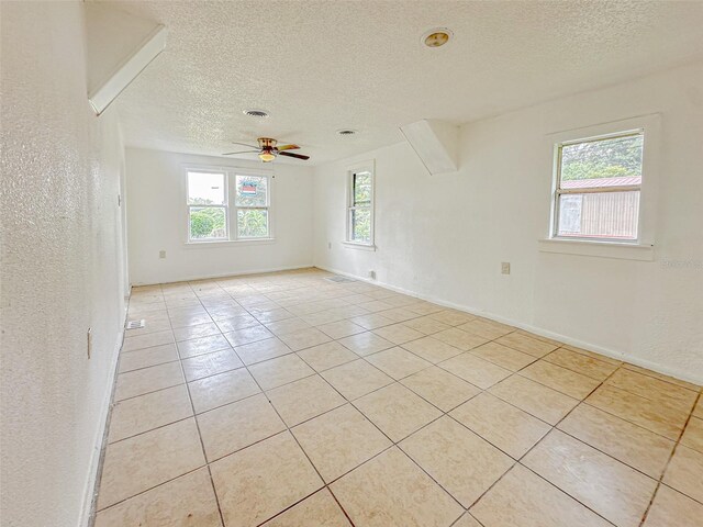 tiled empty room with ceiling fan and a textured ceiling