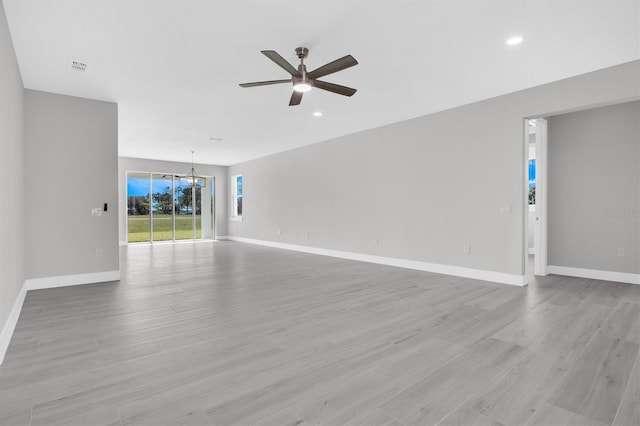 empty room featuring ceiling fan with notable chandelier and light hardwood / wood-style flooring