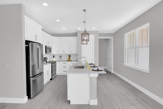 kitchen featuring white cabinets, sink, hanging light fixtures, stainless steel appliances, and a center island with sink