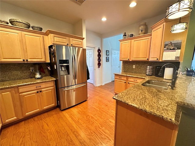 kitchen featuring sink, backsplash, light wood-type flooring, hanging light fixtures, and stainless steel refrigerator with ice dispenser