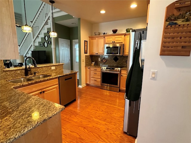 kitchen with pendant lighting, stainless steel appliances, sink, tasteful backsplash, and light hardwood / wood-style floors