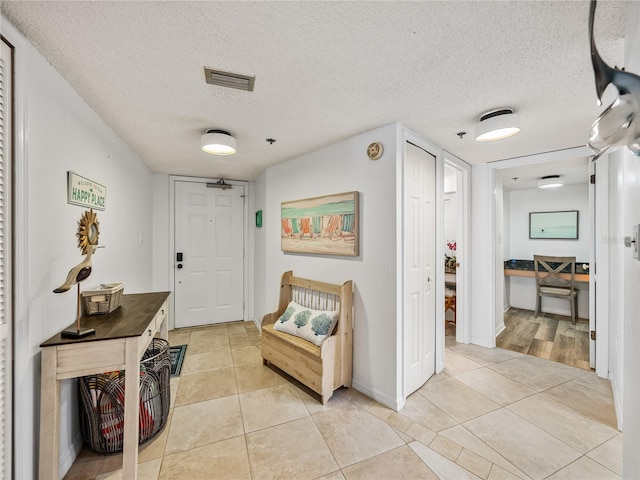 hall with a textured ceiling and light tile flooring