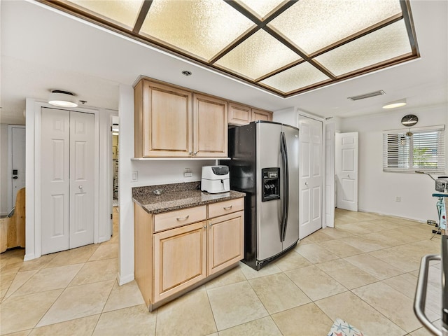 kitchen with stainless steel fridge with ice dispenser, light brown cabinets, light tile floors, and dark stone counters