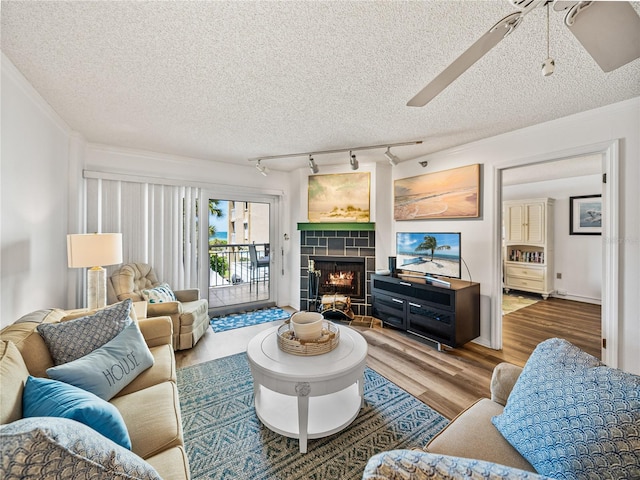 living room with a textured ceiling, light hardwood / wood-style flooring, a tile fireplace, ceiling fan, and track lighting