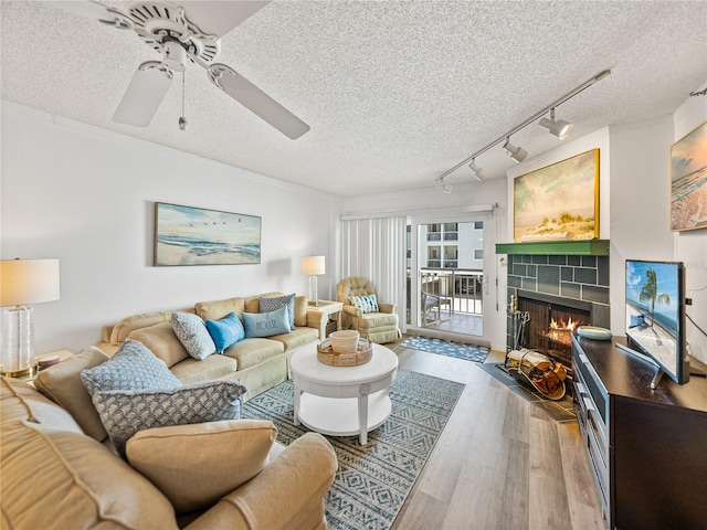 living room with ceiling fan, track lighting, wood-type flooring, a textured ceiling, and a fireplace