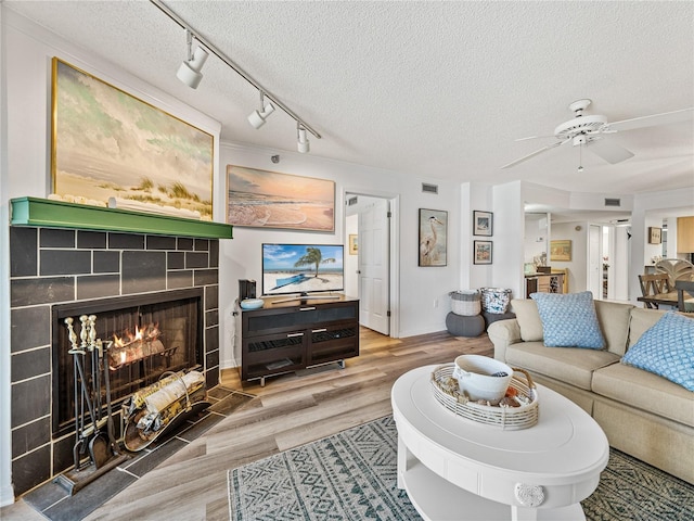 living room featuring a tiled fireplace, hardwood / wood-style floors, rail lighting, ceiling fan, and a textured ceiling