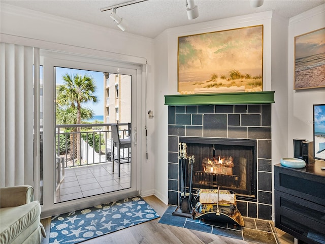 doorway to outside with a textured ceiling, track lighting, light hardwood / wood-style floors, and a tiled fireplace