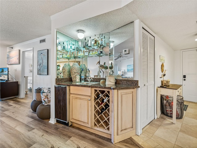 bar featuring ceiling fan, light brown cabinets, a textured ceiling, sink, and dark stone countertops