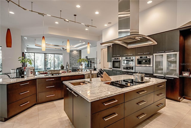 kitchen featuring a large island with sink, black electric cooktop, island range hood, and hanging light fixtures