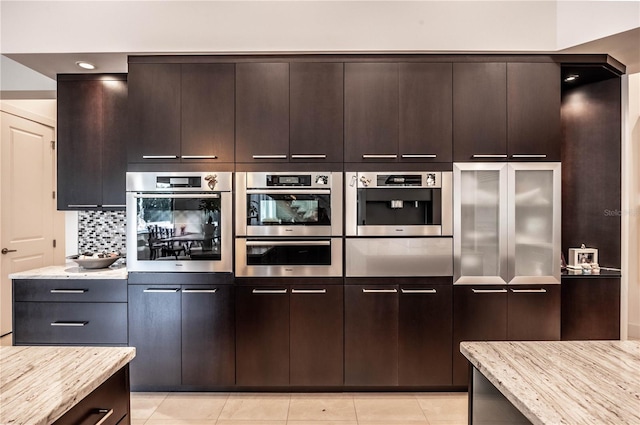 kitchen with stainless steel double oven, dark brown cabinets, backsplash, and light stone counters