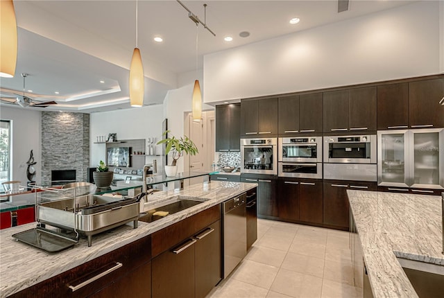 kitchen featuring stainless steel appliances, light stone counters, a fireplace, a raised ceiling, and pendant lighting