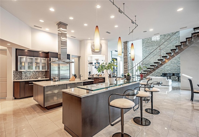 kitchen featuring dark brown cabinets, light stone counters, light tile flooring, and a towering ceiling