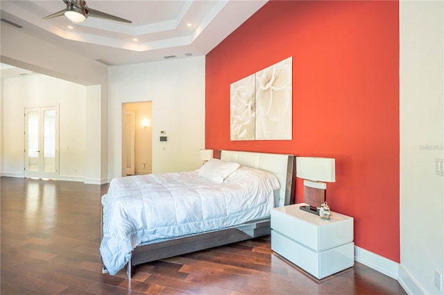 bedroom with dark wood-type flooring, ceiling fan, and a raised ceiling