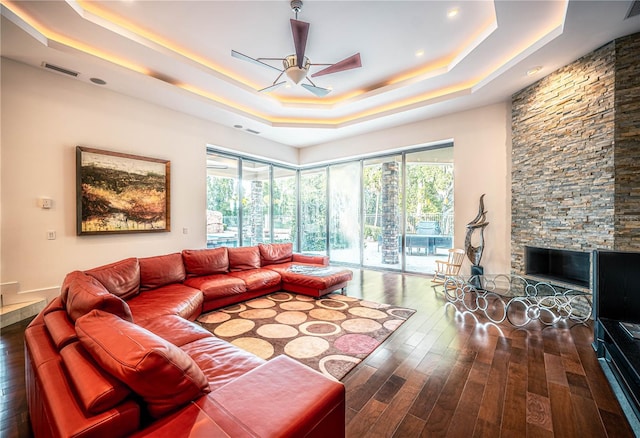 living room with dark hardwood / wood-style flooring, ceiling fan, a fireplace, and a tray ceiling