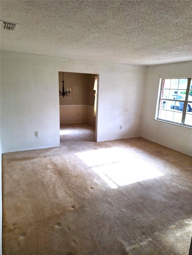 empty room with carpet, a textured ceiling, and a notable chandelier