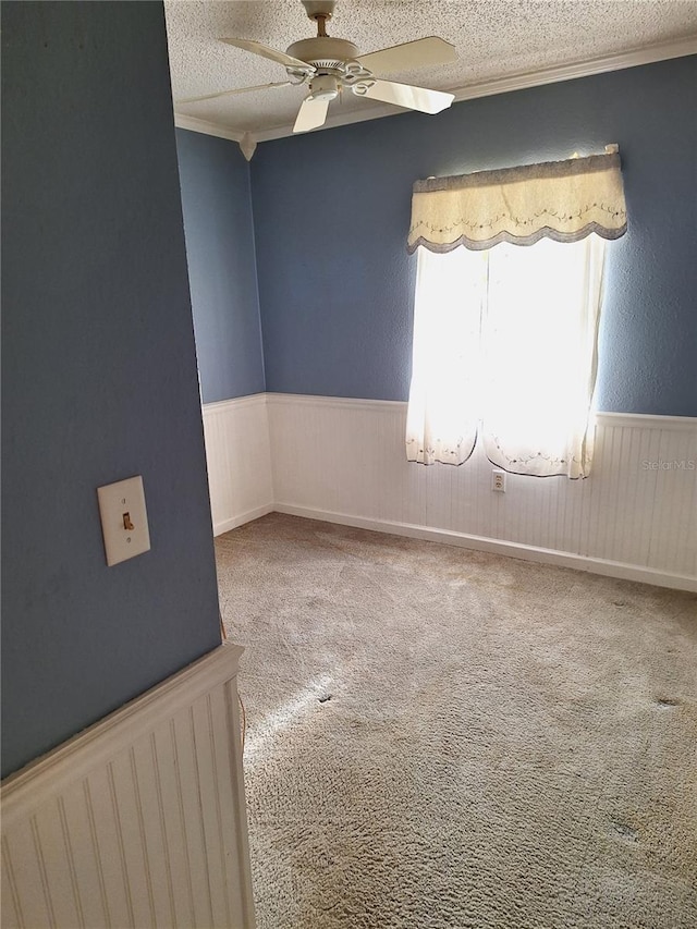 empty room with a textured ceiling, carpet floors, ceiling fan, and ornamental molding