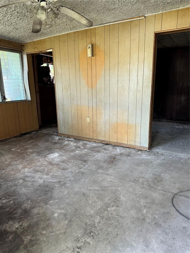 unfurnished room featuring concrete flooring, ceiling fan, and wooden walls