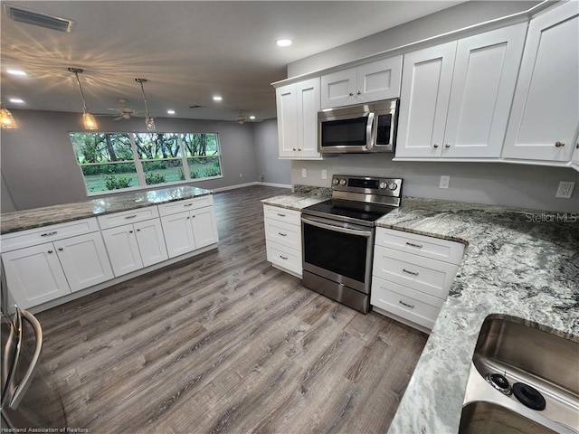 kitchen featuring appliances with stainless steel finishes, light wood-type flooring, white cabinetry, decorative light fixtures, and light stone countertops