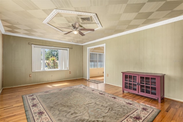 empty room featuring ceiling fan, wood walls, wood-type flooring, and ornamental molding