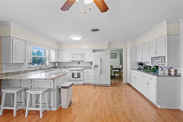 kitchen featuring kitchen peninsula, light hardwood / wood-style flooring, white appliances, sink, and a breakfast bar