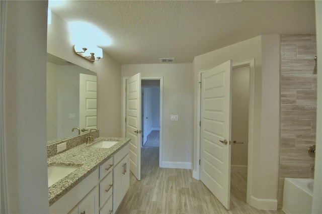 bathroom featuring a sink, a tub, wood finished floors, a textured ceiling, and visible vents