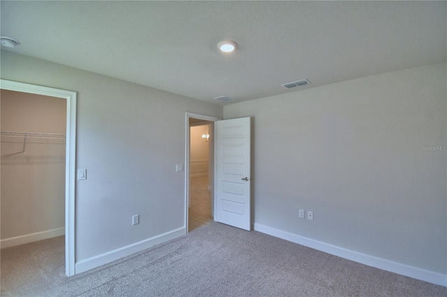 unfurnished bedroom with a closet, carpet floors, a spacious closet, baseboards, and visible vents