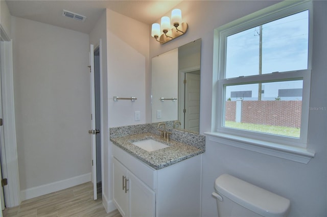 bathroom with vanity, toilet, baseboards, visible vents, and wood finished floors