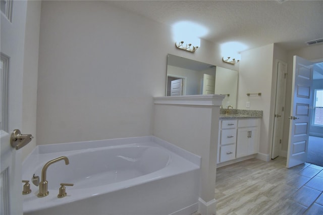 full bathroom with a textured ceiling, visible vents, vanity, and a garden tub