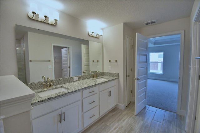 bathroom with a textured ceiling, visible vents, double vanity, a sink, and a walk in closet