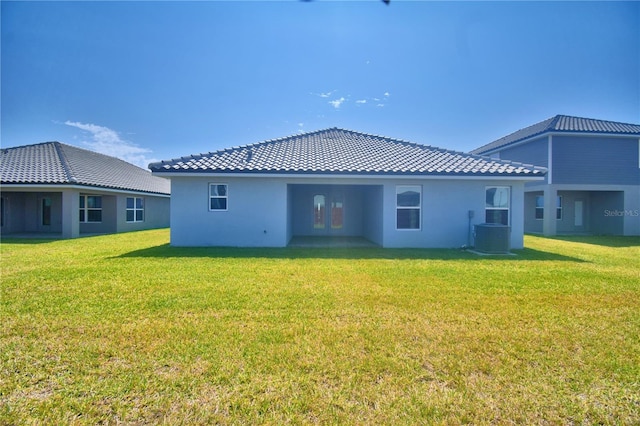rear view of house with central AC unit, a tile roof, stucco siding, and a yard
