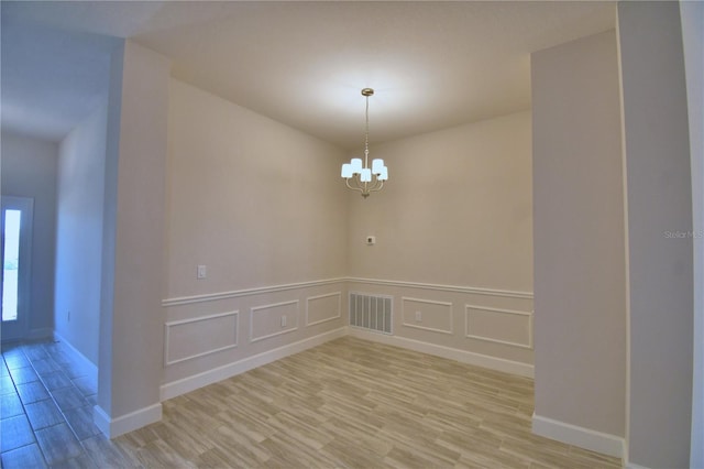 spare room featuring a decorative wall, visible vents, a notable chandelier, and light wood finished floors