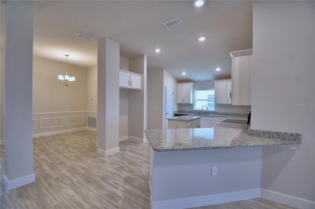 kitchen featuring visible vents, light stone countertops, an inviting chandelier, and a peninsula