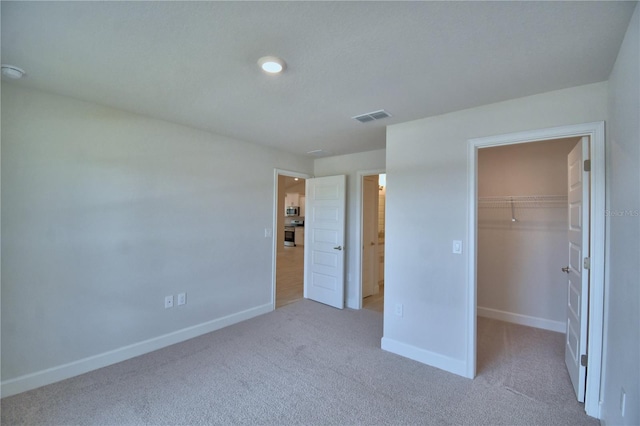 unfurnished bedroom featuring baseboards, visible vents, a walk in closet, and carpet