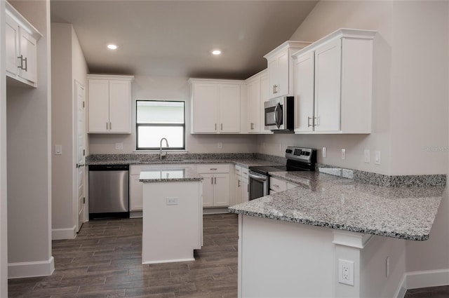 kitchen with kitchen peninsula, stainless steel appliances, light stone countertops, white cabinets, and sink