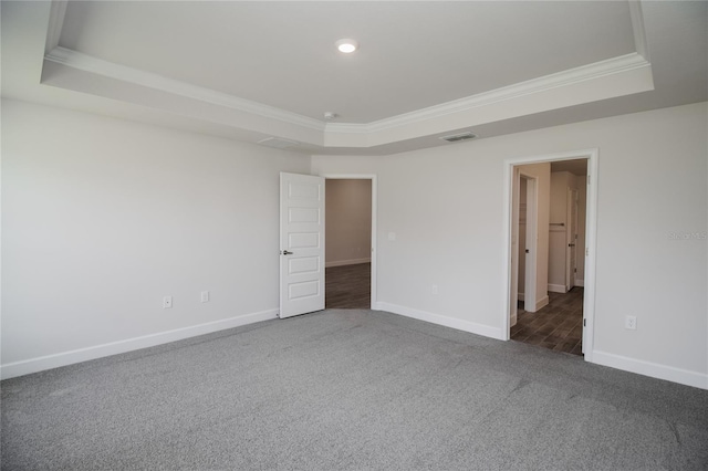 spare room with dark colored carpet, a raised ceiling, and crown molding