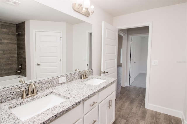 bathroom featuring dual sinks, oversized vanity, tiled shower / bath combo, a notable chandelier, and hardwood / wood-style flooring