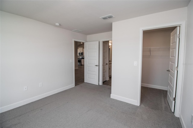 unfurnished bedroom featuring dark carpet, a walk in closet, and a closet